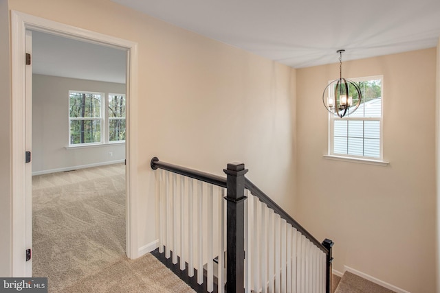 stairway with carpet floors, a healthy amount of sunlight, and a notable chandelier