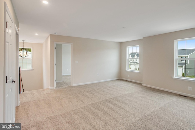 spare room with a wealth of natural light, light carpet, and an inviting chandelier