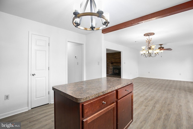 kitchen with hardwood / wood-style flooring, beam ceiling, decorative light fixtures, ceiling fan with notable chandelier, and a center island