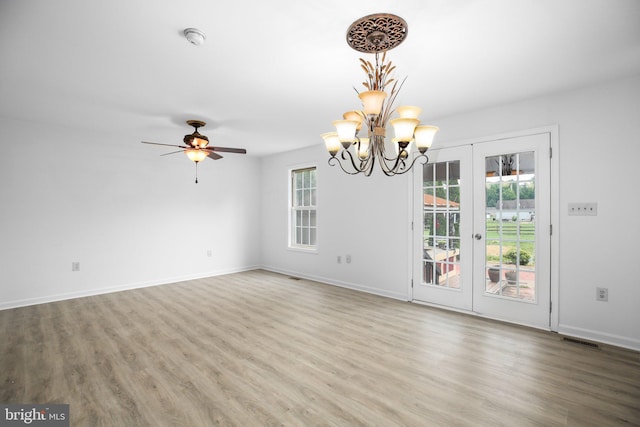 empty room with wood-type flooring, ceiling fan with notable chandelier, and french doors