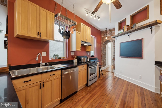 kitchen featuring appliances with stainless steel finishes, light wood-type flooring, brick wall, sink, and pendant lighting