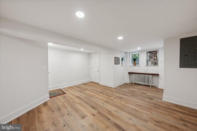 basement featuring electric panel, light hardwood / wood-style floors, and radiator