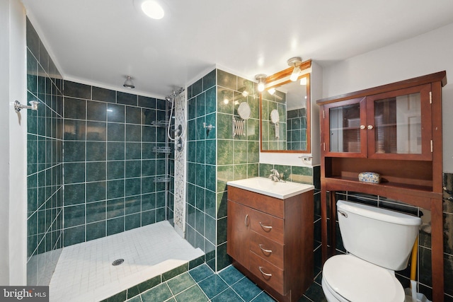 bathroom with vanity, tile patterned floors, toilet, tile walls, and a tile shower