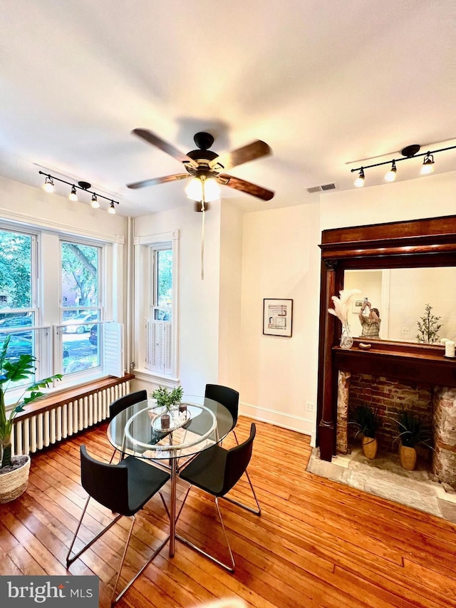 dining space with a fireplace, light hardwood / wood-style flooring, and ceiling fan