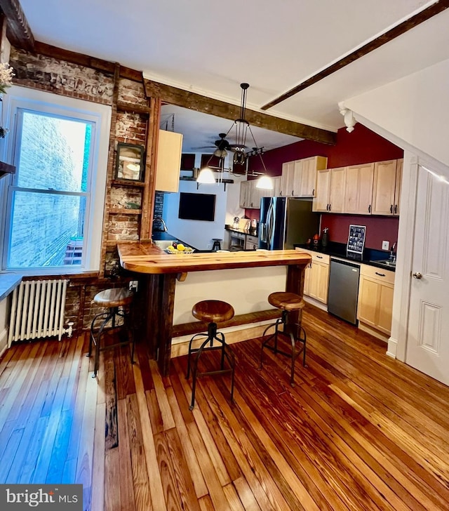 kitchen with radiator heating unit, beamed ceiling, hardwood / wood-style floors, decorative light fixtures, and appliances with stainless steel finishes