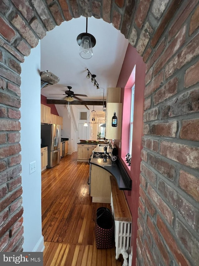 kitchen with stainless steel appliances, rail lighting, brick wall, and light hardwood / wood-style floors