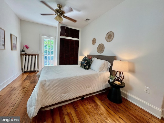 bedroom with access to outside, ceiling fan, radiator heating unit, and wood-type flooring