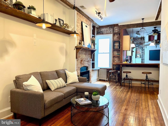 living room with radiator heating unit, brick wall, wood-type flooring, track lighting, and a fireplace