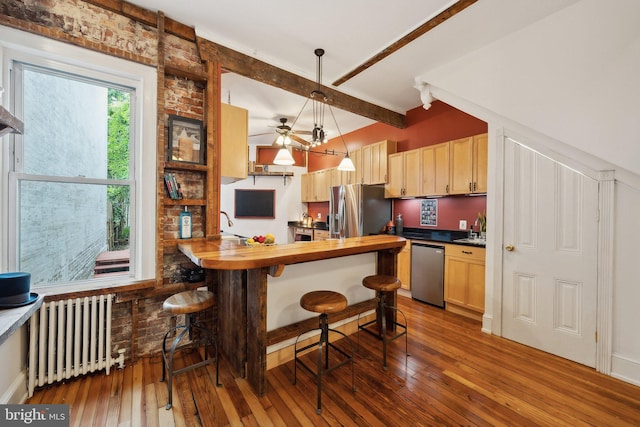 kitchen featuring light brown cabinetry, appliances with stainless steel finishes, radiator, pendant lighting, and butcher block counters