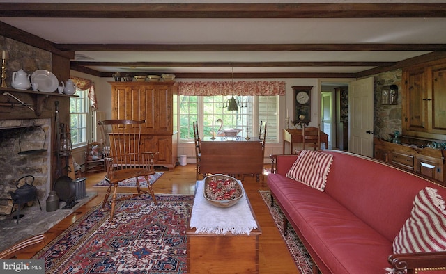 living room featuring hardwood / wood-style flooring, plenty of natural light, a stone fireplace, and beamed ceiling