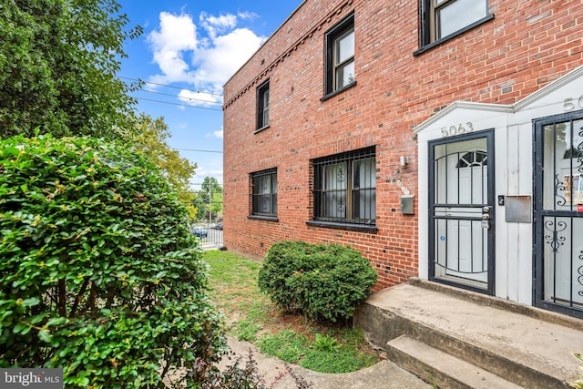 doorway to property featuring brick siding and fence