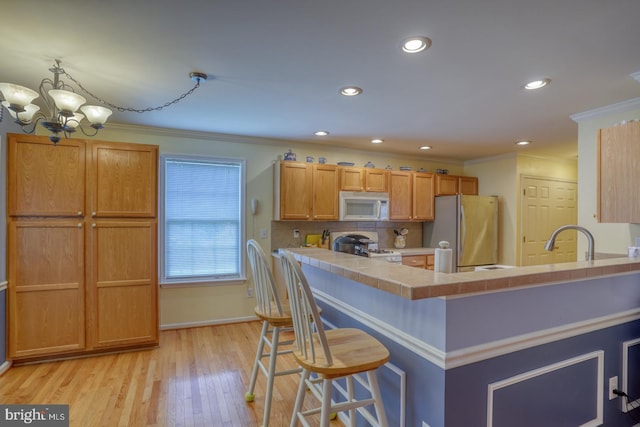 kitchen with white appliances, an inviting chandelier, light wood-type flooring, ornamental molding, and a kitchen bar