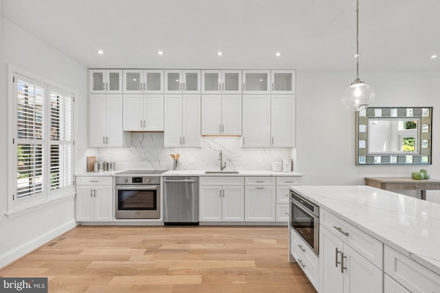 kitchen with white cabinets, sink, hanging light fixtures, light stone countertops, and stainless steel appliances