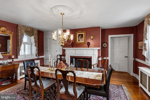 dining space with a chandelier, wood-type flooring, radiator heating unit, and a textured ceiling