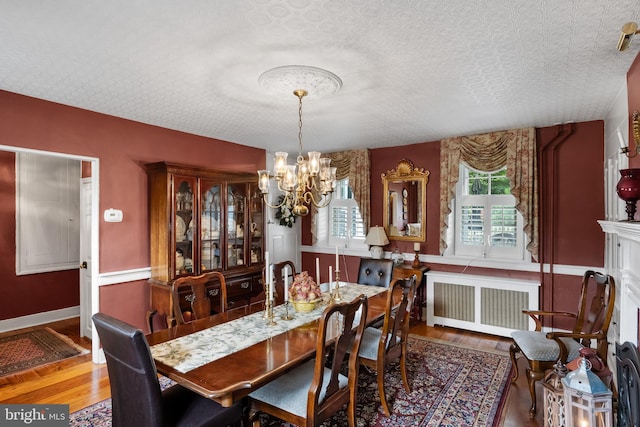 dining space featuring a chandelier, radiator heating unit, a healthy amount of sunlight, and wood-type flooring