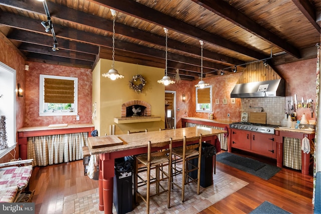 kitchen featuring a wealth of natural light, dark wood-type flooring, beamed ceiling, range hood, and a kitchen bar