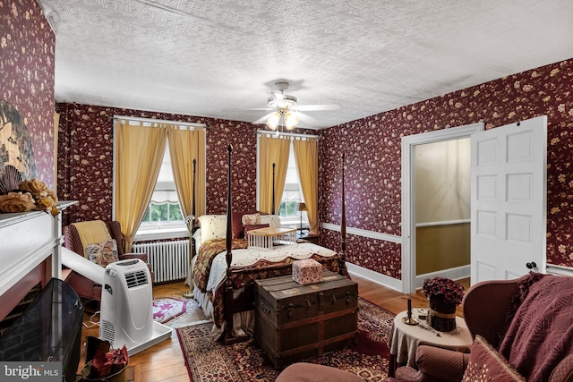 bedroom with ceiling fan, radiator heating unit, a textured ceiling, and hardwood / wood-style flooring