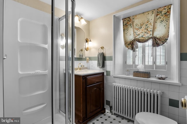 bathroom with vanity, radiator, toilet, tile walls, and a shower with shower door