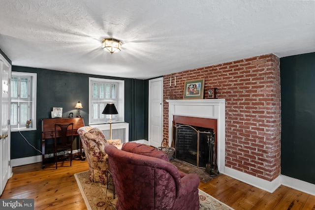 living room with hardwood / wood-style floors, a textured ceiling, and a brick fireplace