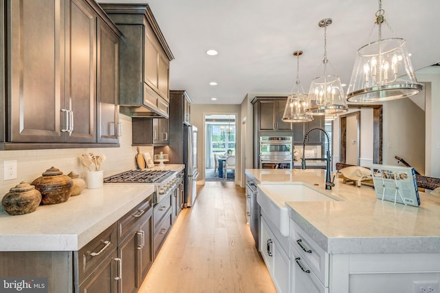 kitchen with light stone countertops, sink, hanging light fixtures, light wood-type flooring, and appliances with stainless steel finishes