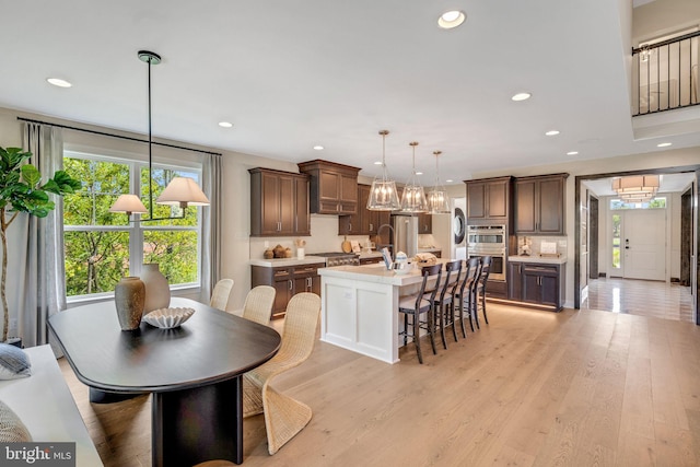 kitchen featuring dark brown cabinetry, a breakfast bar, pendant lighting, a center island with sink, and light wood-type flooring