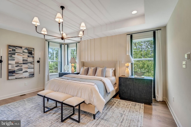 bedroom with light hardwood / wood-style floors, an inviting chandelier, and a tray ceiling