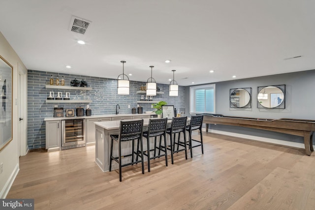 bar with white cabinetry, sink, hanging light fixtures, wine cooler, and light hardwood / wood-style flooring