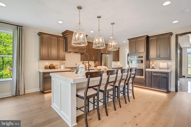 kitchen with a center island with sink, light wood-type flooring, stainless steel appliances, and hanging light fixtures