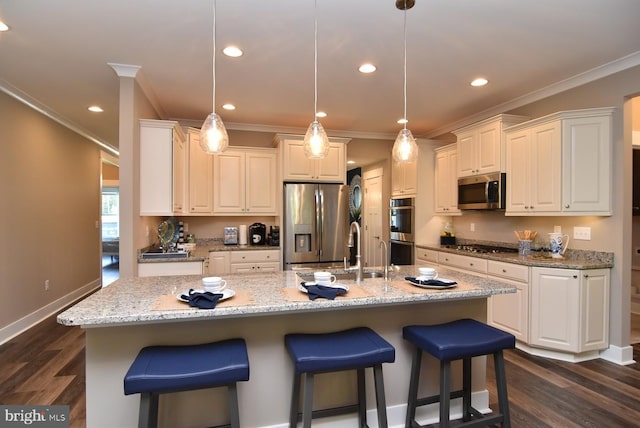 kitchen featuring white cabinets, appliances with stainless steel finishes, hanging light fixtures, and a kitchen island with sink