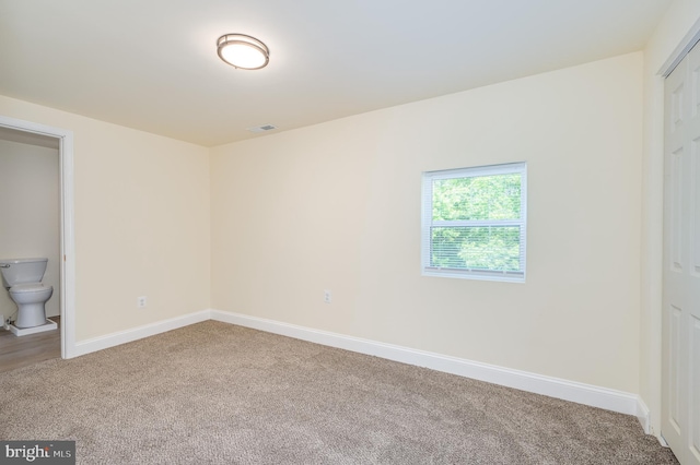 unfurnished bedroom with carpet flooring, a closet, and ensuite bath