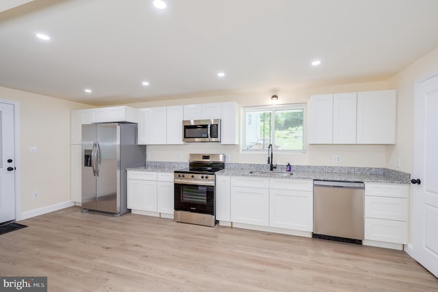 kitchen with light stone countertops, appliances with stainless steel finishes, sink, white cabinets, and light hardwood / wood-style floors