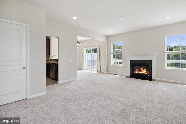 unfurnished living room featuring light carpet, baseboards, a wealth of natural light, and a glass covered fireplace