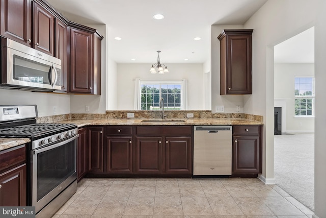 kitchen with dark brown cabinets, appliances with stainless steel finishes, a sink, and light stone counters