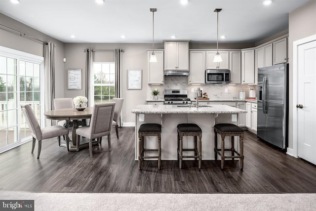 kitchen featuring a kitchen island with sink, sink, decorative light fixtures, dark hardwood / wood-style flooring, and stainless steel appliances