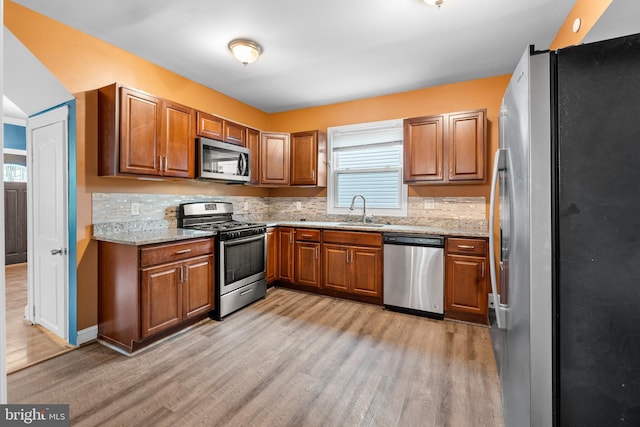 kitchen with appliances with stainless steel finishes, backsplash, light stone counters, sink, and light hardwood / wood-style floors