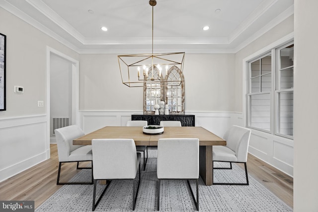 dining space with a tray ceiling, a chandelier, ornamental molding, and light wood-type flooring