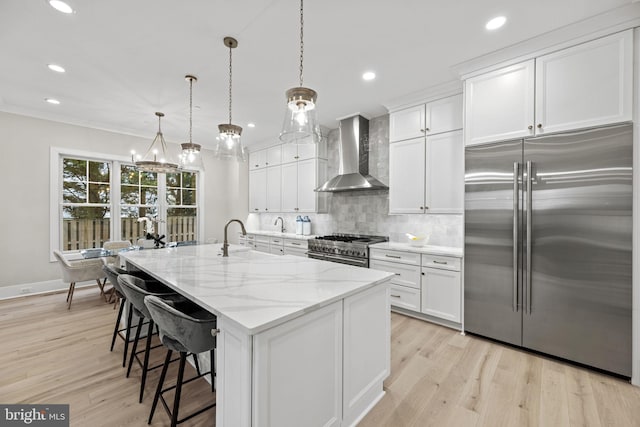 kitchen featuring high quality appliances, sink, hanging light fixtures, wall chimney exhaust hood, and white cabinetry