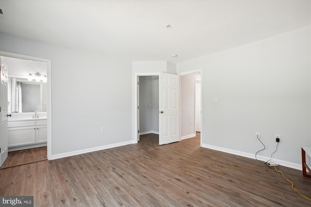 unfurnished bedroom featuring a spacious closet, ensuite bathroom, and hardwood / wood-style floors