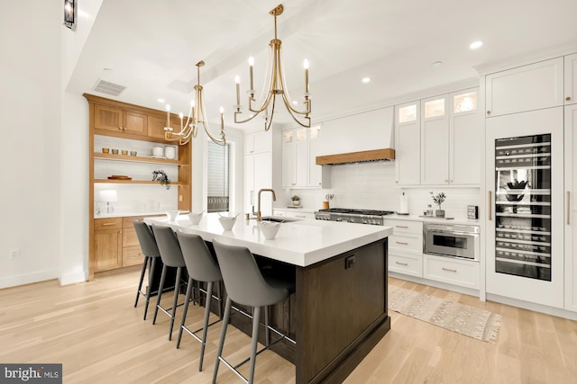 kitchen featuring custom exhaust hood, white cabinetry, and a center island with sink