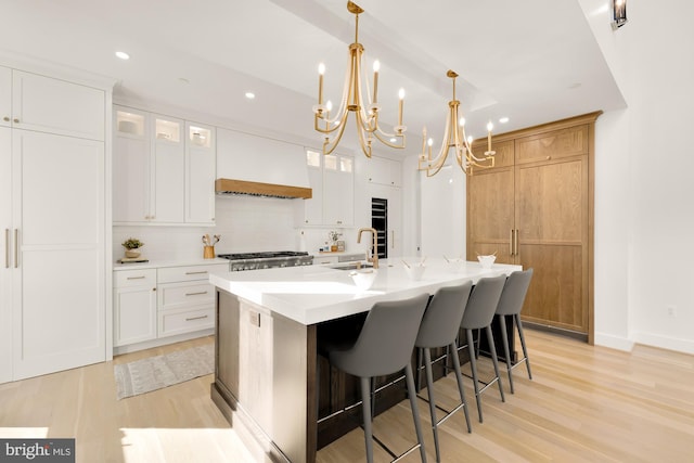 kitchen with custom exhaust hood, white cabinets, hanging light fixtures, and an island with sink