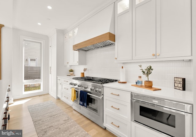 kitchen with white cabinets, decorative backsplash, light wood-type flooring, and appliances with stainless steel finishes