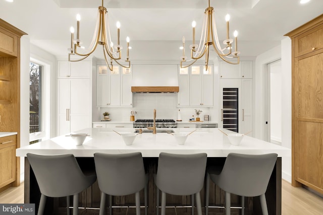 kitchen with decorative light fixtures, white cabinets, a large island, backsplash, and premium range hood