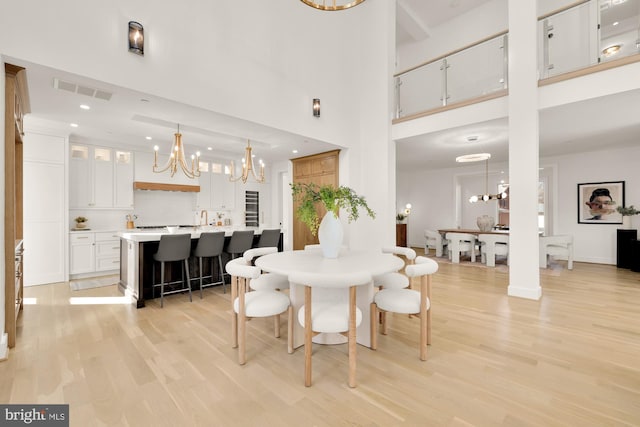 dining space featuring light hardwood / wood-style flooring, an inviting chandelier, and a towering ceiling