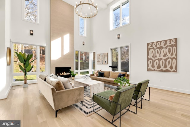 living room with a towering ceiling, a fireplace, an inviting chandelier, and light wood-type flooring