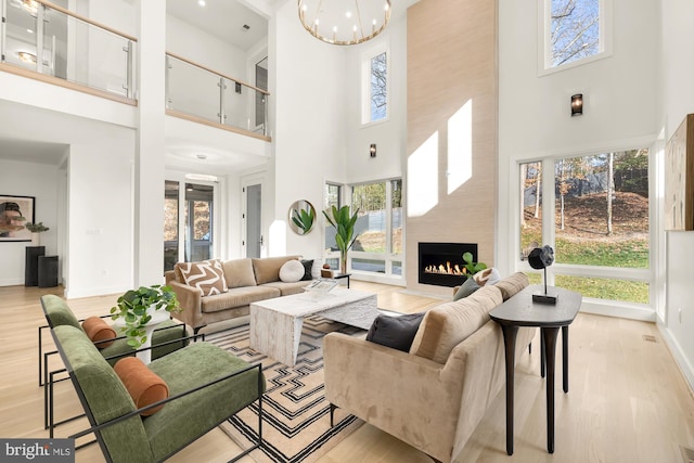 living room featuring a high ceiling, an inviting chandelier, a large fireplace, and light wood-type flooring