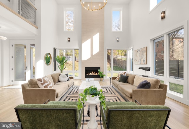 living room featuring a large fireplace, a towering ceiling, light wood-type flooring, and an inviting chandelier