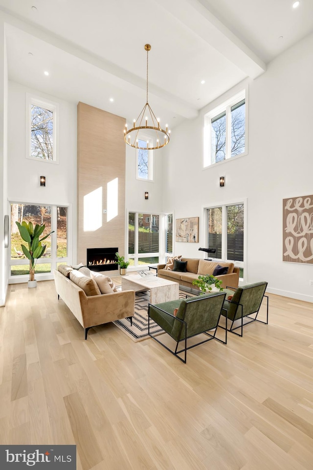 living room with a fireplace, an inviting chandelier, light wood-type flooring, a high ceiling, and beam ceiling