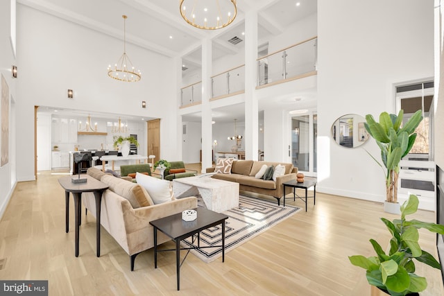 living room featuring a towering ceiling, beam ceiling, a notable chandelier, and light hardwood / wood-style flooring