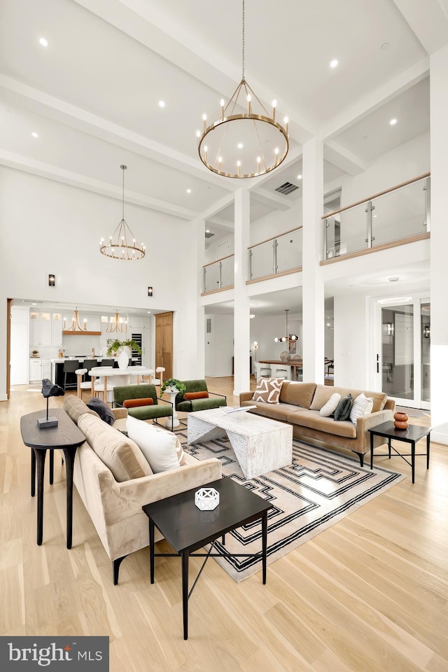 living room featuring light hardwood / wood-style floors, an inviting chandelier, a high ceiling, and beam ceiling