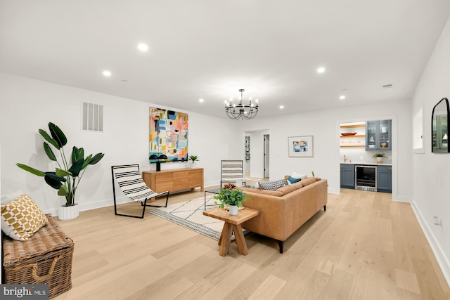 living room with an inviting chandelier, wine cooler, and light hardwood / wood-style flooring